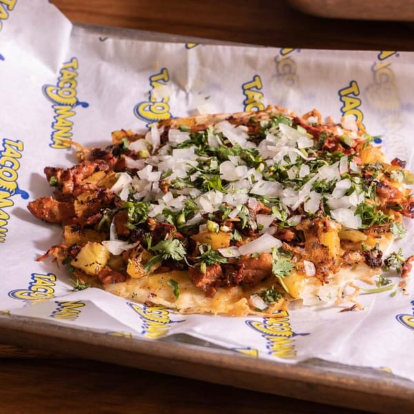 TacoMania al pastor taco with pineapple, onions, and cilantro on branded parchment paper.