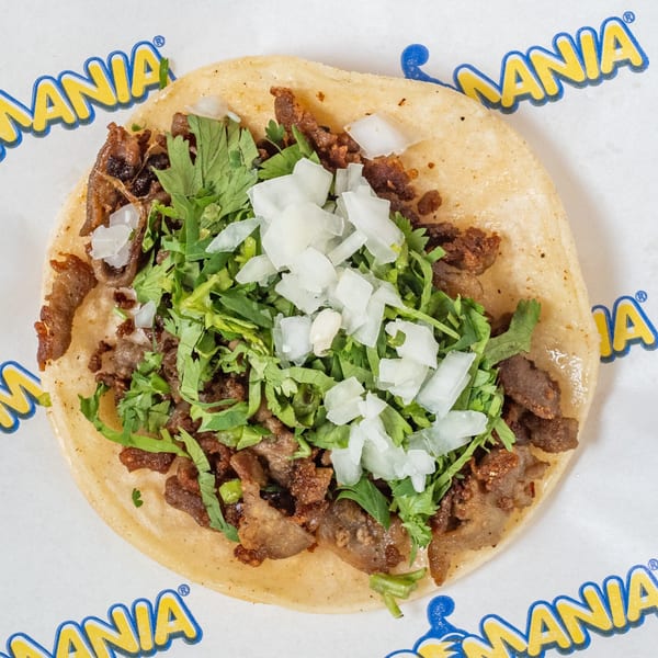 Overhead view of a TacoMania taco with carne asada, cilantro, and diced onions on a corn tortilla.
