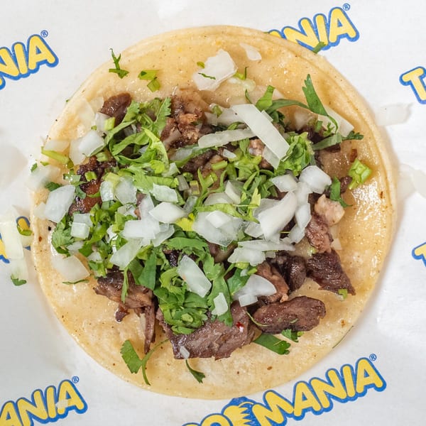 Overhead view of a TacoMania taco with carne asada, cilantro, and diced onions on a tortilla.