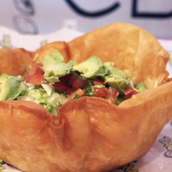 A TacoMania taco salad in a crispy fried tortilla bowl, topped with avocado, tomato, and lettuce.