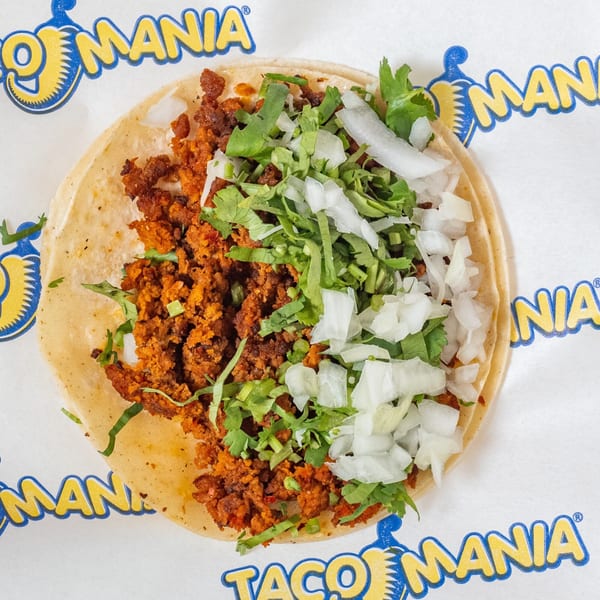 TacoMania taco with seasoned meat, cilantro, and diced onions on a white branded wrapper.