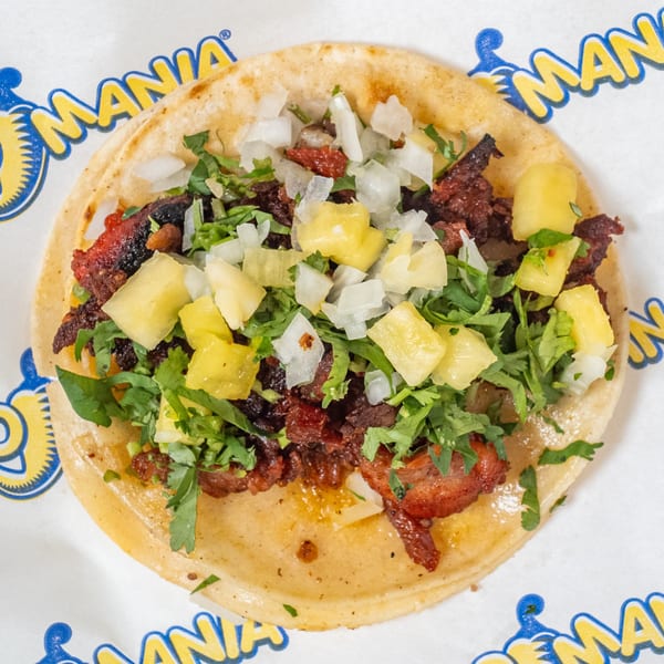 TacoMania al pastor taco with pork, pineapple, onions, and cilantro on a corn tortilla.