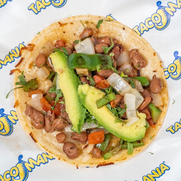 TacoMania taco with pinto beans, avocado slices, green peppers, and onions on a white wrapper.
