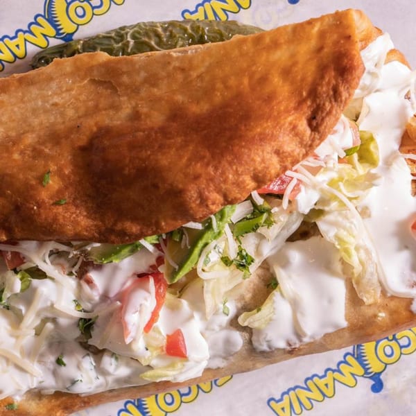 A close-up of a TacoMania taco, filled with lettuce, tomatoes, avocado, cheese, and sour cream.