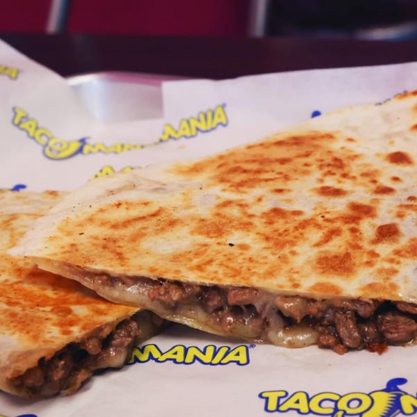Two golden-brown TacoMania quesadillas filled with melted cheese and savory meat, served on branded paper.